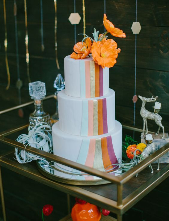 a colorful and fun wedding cake in white with bright blooms and bold orange flowers on top is a lovely and fun idea for a 70s wedding