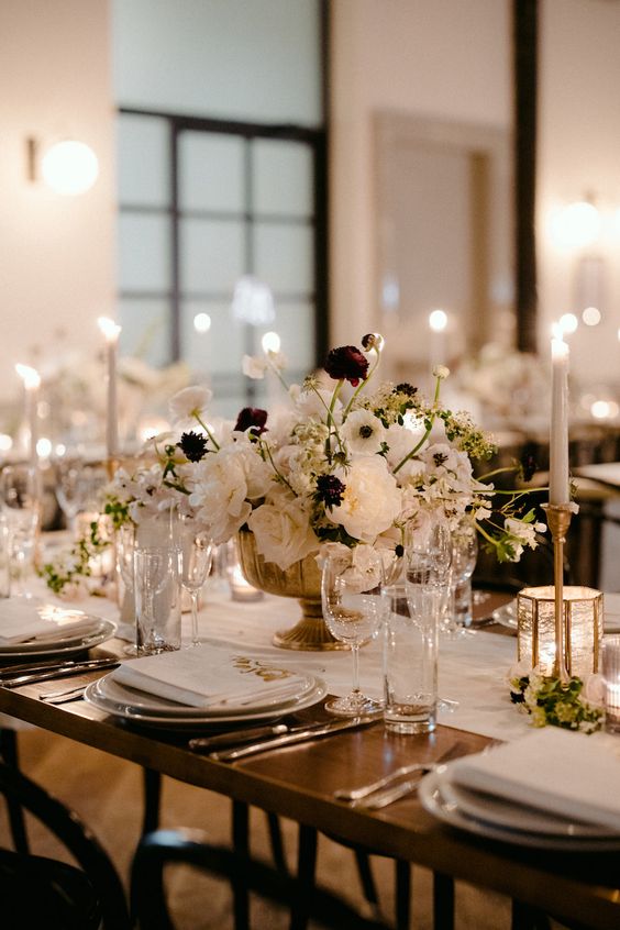 a beautiful and refined wedding tablescape with white linens, white florals with burgundy touches and neutral candles