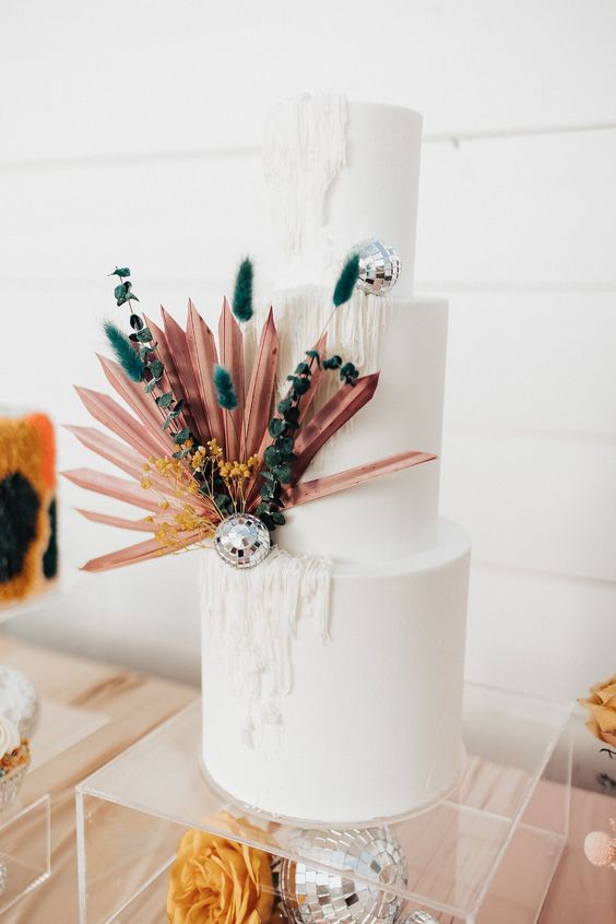 a statement disco wedding cake in white, with yarn like detailing, with colorful spikes, a mauve frond and some leaves and disco balls