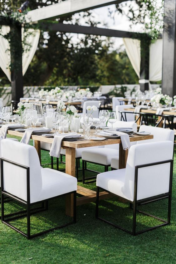 a modern lux wedding reception space with wooden tables, neutral linens, white blooms and candles plus chic upholstered chairs