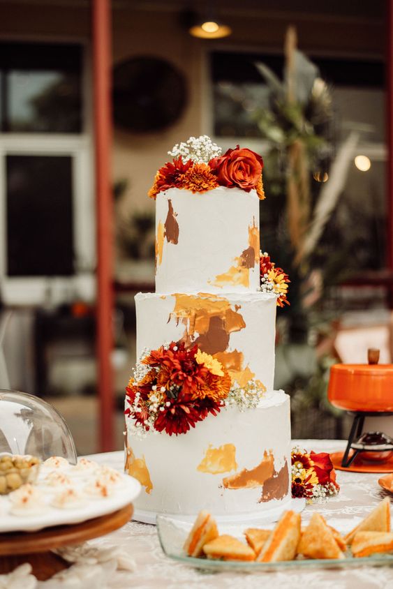 23 a pretty and bright wedding cake in white, with earthy tone brushstrokes and bold fresh blooms and baby’s breath for a 70s wedding