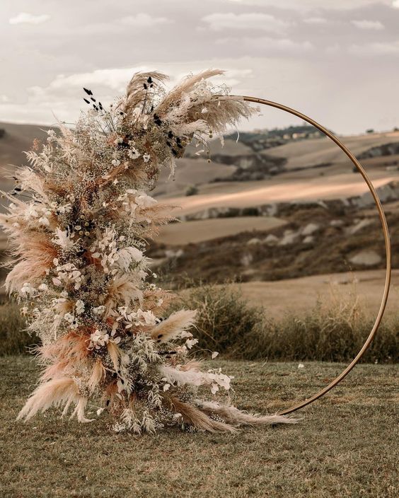 a boho round wedding arch with one side decorated with pampas grass and other grasses, white and dried blooms
