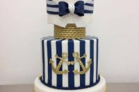 a bold and refined nautical wedding cake with white, navy and white striped tiers, gold ropes, gold anchors, white sugar blooms and pearls