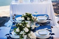 a bold nautical glam wedding tablescape with a navy sequin tablecloth, white florals, seashells and corals and white plates