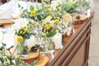 a bright and cool cluster wedding centerpiece of yellow berries and billy balls, white blooms and greenery, candles and pinecones