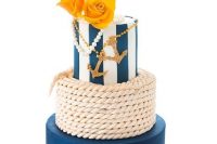 a bright nautical wedding cake with a rope, a navy and a striped tier, gold glitter anchors, pearls and yellow roses is a bold and cool idea
