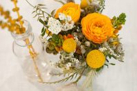 a bright wedding centerpiece of yellow and white blooms, berries and greenery is a pretty idea for a summer or fall wedding