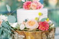 a chic rustic wedding cake with billy balls, peachy and coral blooms, a laser cut topper served on a tree stump