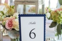 a classic nautical wedding centerpiece of a shabby chic candle lantern, white and pink blooms and greenery, a navy table number