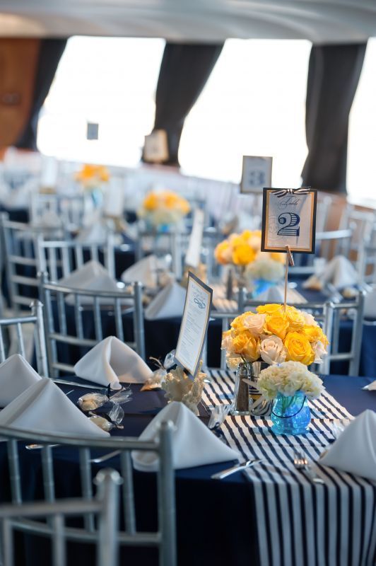 a classic nautical wedding tablescape with a navy tablecloth, a striped runner, neutral and yellow blooms and white napkins