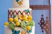 a colorful wedding cake with Moroccan patterns, bright butterflies, grreenery and billy balls plus lace ribbon is chic and bold
