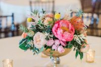 a colorful wedding centerpiece of a brass bowl, bold pink and blush blooms, greenery and billy balls for spring or summer
