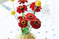 a colorful wedding centerpiece of bold red blooms and billy balls plus a catchy yellow vase for a summer or fall wedding