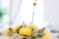 a creative wedding centerpiece of pale leaves, yellow blooms and billy balls is a pretty idea for a spring or summer wedding