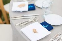 a cute nautical wedding tablescape with a grey tablecloth, white napkins, navy anchor ones, white porcelain is simple and lovely