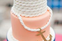 a gorgeous nautical wedding cake with a blue striped tier, a peachy one and a white rope one plus a gold anchor looks cheerful and fun