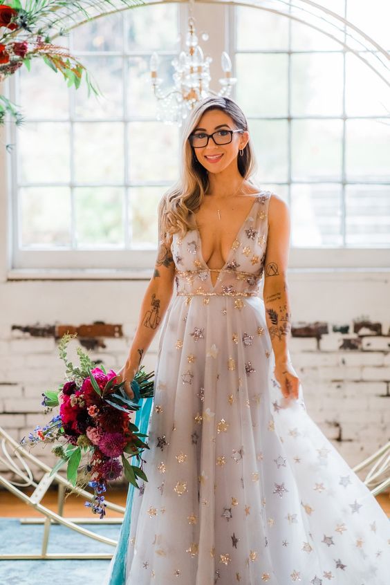 a grey A-line wedding dress with a plunnging neckline, thick straps and gold foil stars all over the dress