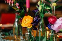a jewel tone cluster wedding centerpiece of greenery and bold blooms plus a pink candle in a gilded candleholder is cool