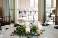 a lovely modern nautical wedding tablescape with a white tablecloth and navy napkins, candles with greenery for a centerpiece