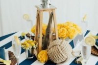 a lovely nautical wedding centerpiece of a lantern with driftwood, yellow blooms, a rope ball and matching woven placemats