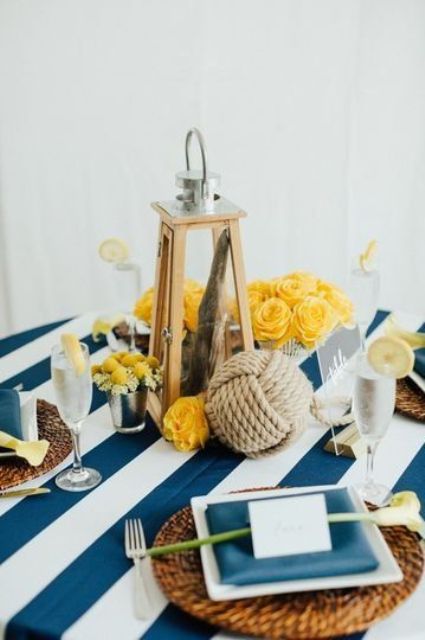 a lovely nautical wedding centerpiece of a lantern with driftwood, yellow blooms, a rope ball and matching woven placemats