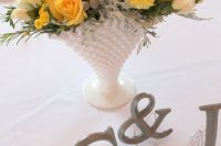 a lovely summer wedding centerpiece of yellow and white blooms, billy balls and greenery in a chic white vase