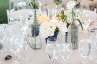 a lovely wedding tablescape with white linens, neutral blooms and a candle, pebbles and greenery, navy vases for a nautical wedding