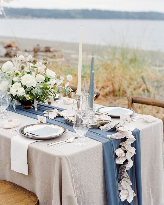 a modern and sophisticated nautical wedding tablescape with a neutral tablecloth and a blue runner, white florals and blue and white candles