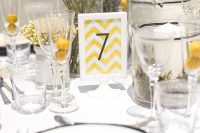 a modern wedding centerpiece of billy balls in a clear vase, with a chevron table number and some yellow baby’s breath for addition