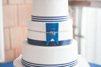a nautical wedding cake with navy stripes, a navy flag, a gold roper, pink blooms and baby’s breath is a gorgeous idea