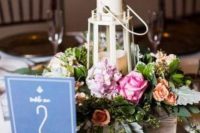 a nautical wedding centerpiece of a wooden box with pink blooms and greenery, a candle lantern shaped as a beacon, a rope knot with a table number