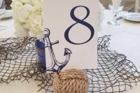 a nautical wedding centerpiece of net, a rope ball, white hydrangeas in a navy vase and a table number wiht an anchor