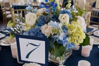 a nautical wedding centerpiece of white and blue blooms and greenery, a rope knot and candles is a stylish and timeless idea