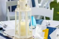 a nautical wedding centerpiece with a beacon candle lantern, a rope number stand, blooms on the table