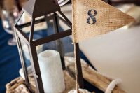 a nautical wedding centerpiece with a candle lantern, driftwood, a burlap flag and a rope knot is a lovely and simple idea