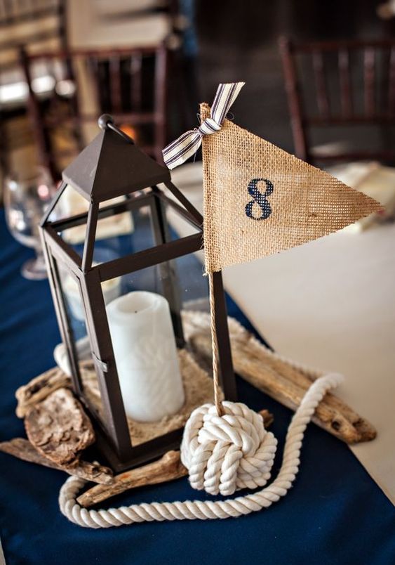 a nautical wedding centerpiece with a candle lantern, driftwood, a burlap flag and a rope knot is a lovely and simple idea