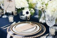 a nautical wedding table setting with a navy tablecloth, white napkins, white floral centerpieces and touches of gold