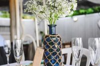 a nautical wedding table setting with woven chargers, turquoise napkins, a blue bottles in a net and white blooms is chic