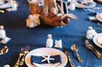 a nautical wedding tablescape with a navy tablecloth and napkins, starfish and corals, driftwood and seashells
