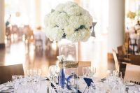 a nautical wedding tablescape with a white tablecloth, a striped runner, a lush white hydrangea centerpiece and white porcelain