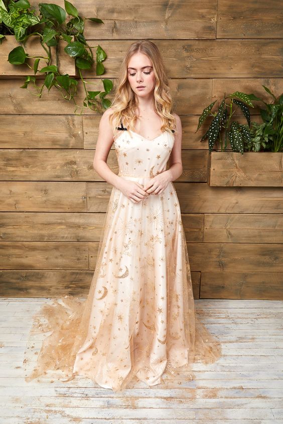 a neutral A-line wedding dress with gold stars and moons, with a train and black spaghetti straps is a very refined idea for a celestial bride