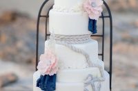 a pretty nautical wedding cake with white tiers, pink sugar blooms and navy doilies, rope and anchors is bold and cool