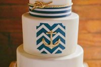 a refined nautical wedding cake with navy stripes and chevrons, gold roper and an anchor, coral blooms is a chic idea for summer