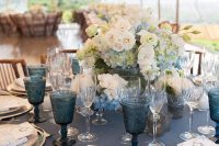 a refined nautical wedding tablescape with a navy tablecloth, gilded chargers and cutlery, white and blue blooms and blue glasses