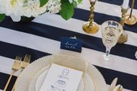 a refined wedding tablescape with a navy and white striped tablecloth, neutral and blush blooms and greenery, touches of gold
