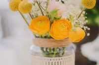 a simple rustic wedding centerpiece of yellow blooms and billy balls, blush roses and baby’s breath in a jar wrapped with twine and lace