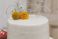 a sleek white wedding cake with billy balls and a pretty bike cake topper for a couple who enjoy riding bikes