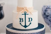 a stylish nautical wedding cake with white textural buttercream, a navy anchor and monograms, neutral rope and lovely cake toppers