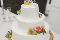 a stylish white buttercream wedding cake with a coral rose, billy balls and greenery and a pretty bicycle wedding cake topper