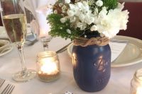 a traditional nautical wedding centerpiece of a navy jar with white blooms and baby’s breath, greenery and rope for decor